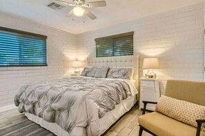 Une chambre à coucher comprenant un lit, une chaise, une table de chevet, une lampe et un ventilateur de plafond.