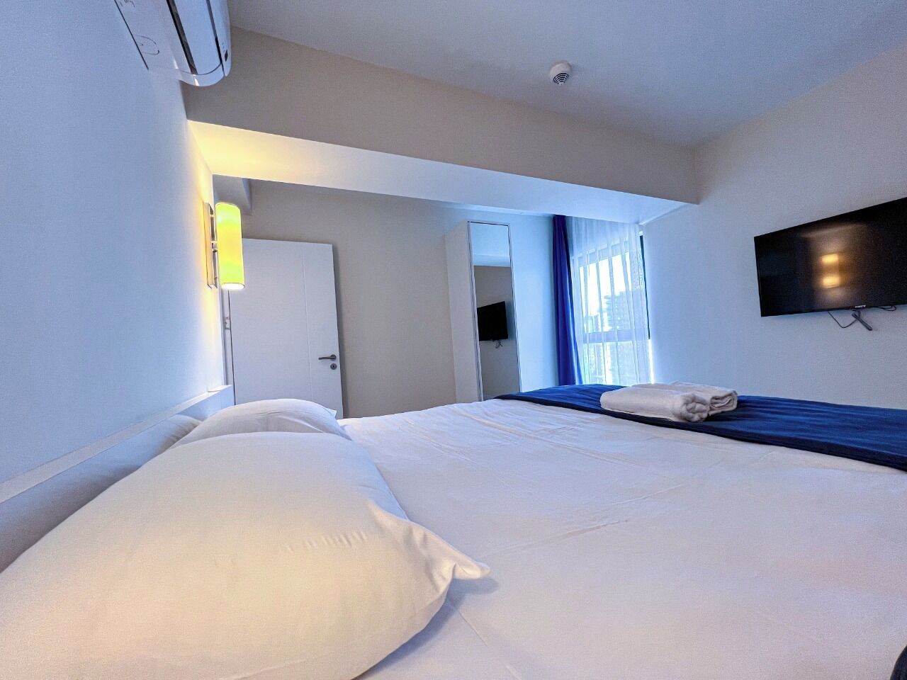 Une chambre d’hôtel avec un lit, un téléviseur fixé au mur et une fenêtre avec des rideaux.