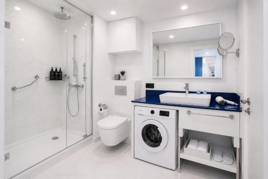 Casa de banho moderna com chuveiro em cabine de vidro, sanita, máquina de lavar roupa e lavatório com bancada azul.
