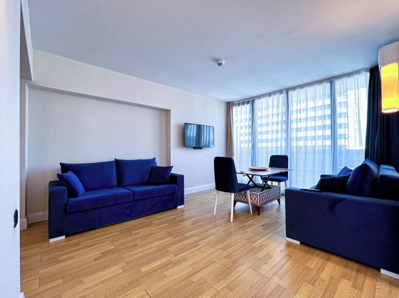 Un salon moderne avec un canapé bleu, une table à manger avec des chaises et un téléviseur fixé au mur.