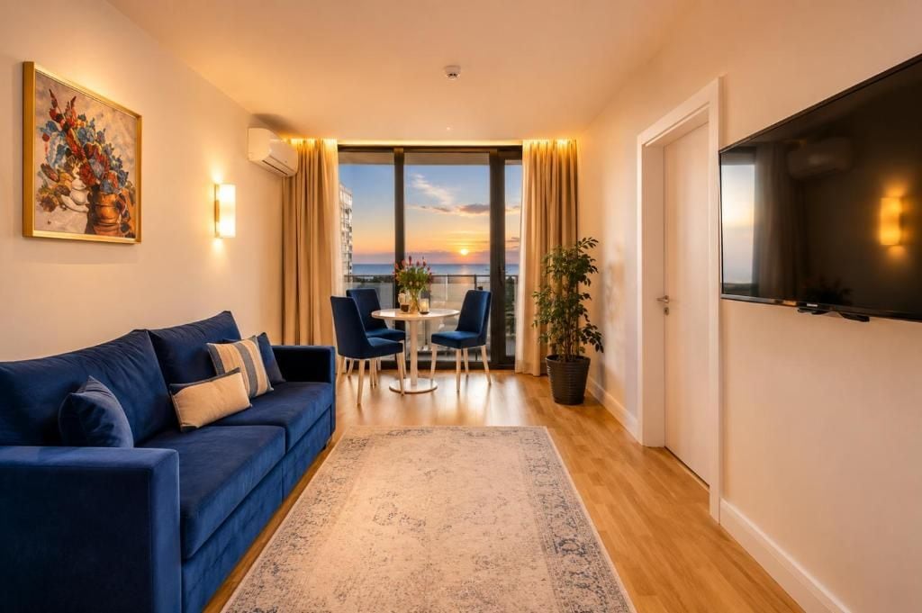Una sala de estar moderna con un sofá, una mesa de comedor con sillas, un ventanal con cortinas y un televisor de pantalla plana montado en la pared.