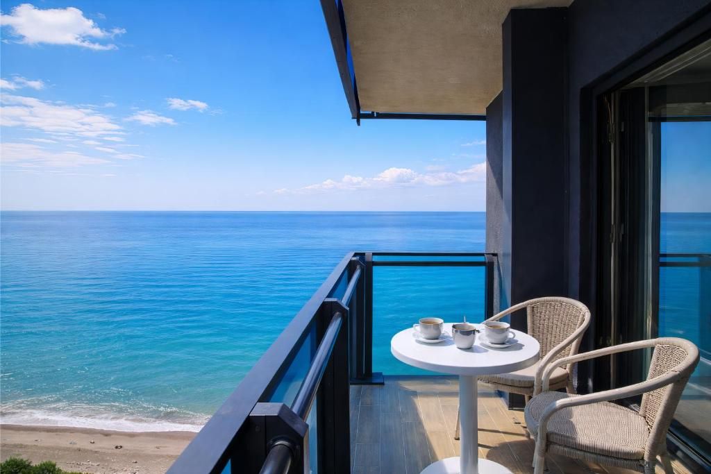A balcony with a view of the ocean, a table with cups, and wicker chairs.