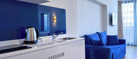 A modern kitchen with a built-in stove, a sink, and a blue sofa in the adjacent living area.