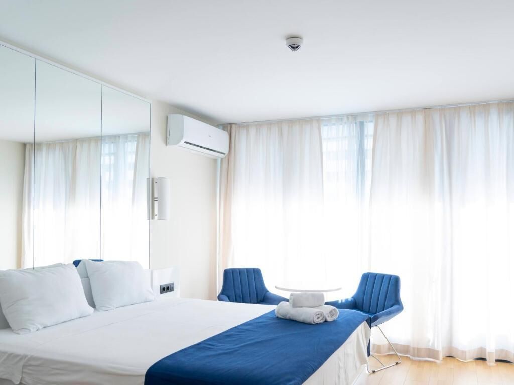 Habitació d'hotel amb llit, dues cadires, taula petita i un mirall gran.