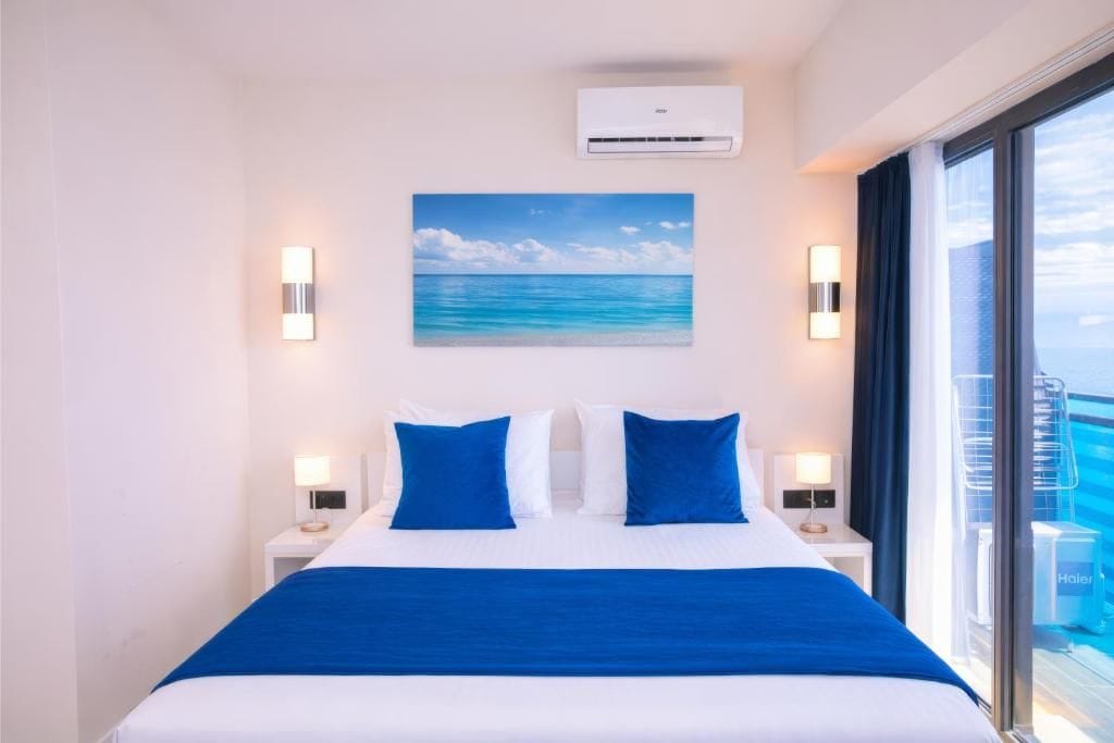 Ein Hotelzimmer mit einem Bett, einem Strandbild, einer Klimaanlage und Meerblick durch ein Fenster.