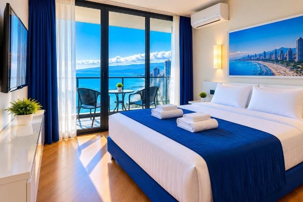A hotel room with a large bed, a balcony with a city view, and a flat-screen TV.