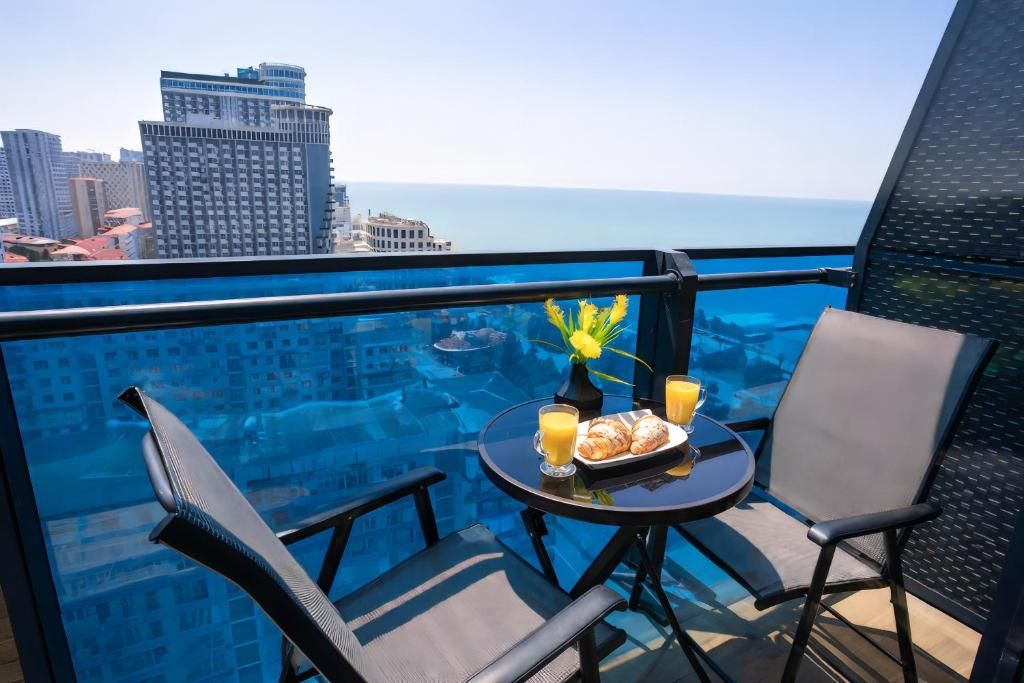 A balcony with a table set for breakfast, overlooking a cityscape and the sea.