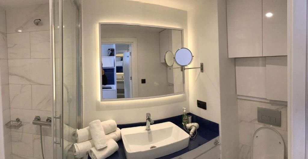 A modern bathroom with a glass shower enclosure, a sink with a mirror above it, and a towel rack with towels.