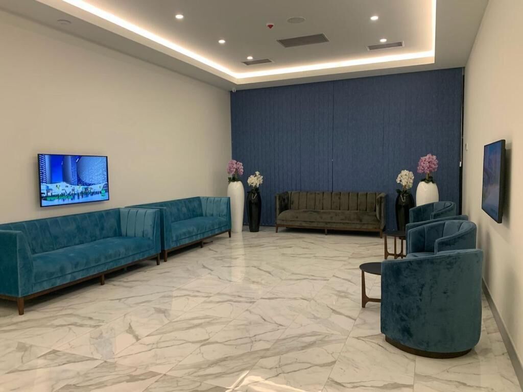 Un espace d’attente moderne avec un canapé bleu, un fauteuil rembourré et un téléviseur fixé au mur.