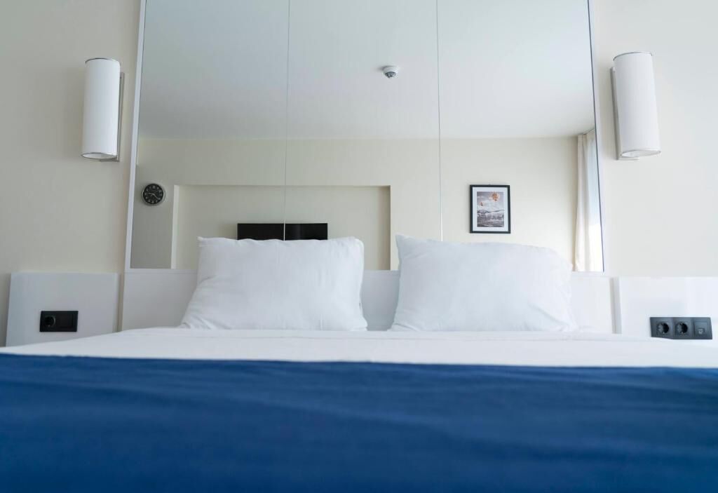 A hotel room with a large bed, white walls, and two wall-mounted light fixtures.