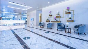 A modern lobby with marble flooring, blue armchairs, and wall-mounted shelves with orchids. - Holiday in orbi city  (Batumi)