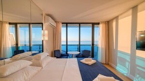 A hotel room with a large bed, a small table, two chairs, and a view of the sea through large windows. - Holiday in orbi city  (Batumi)