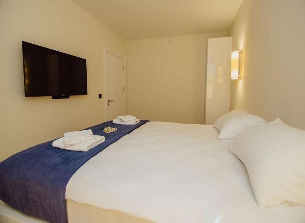 Habitación de hotel con una cama, un televisor de pantalla plana en la pared, una puerta y una lámpara fijada a la pared.