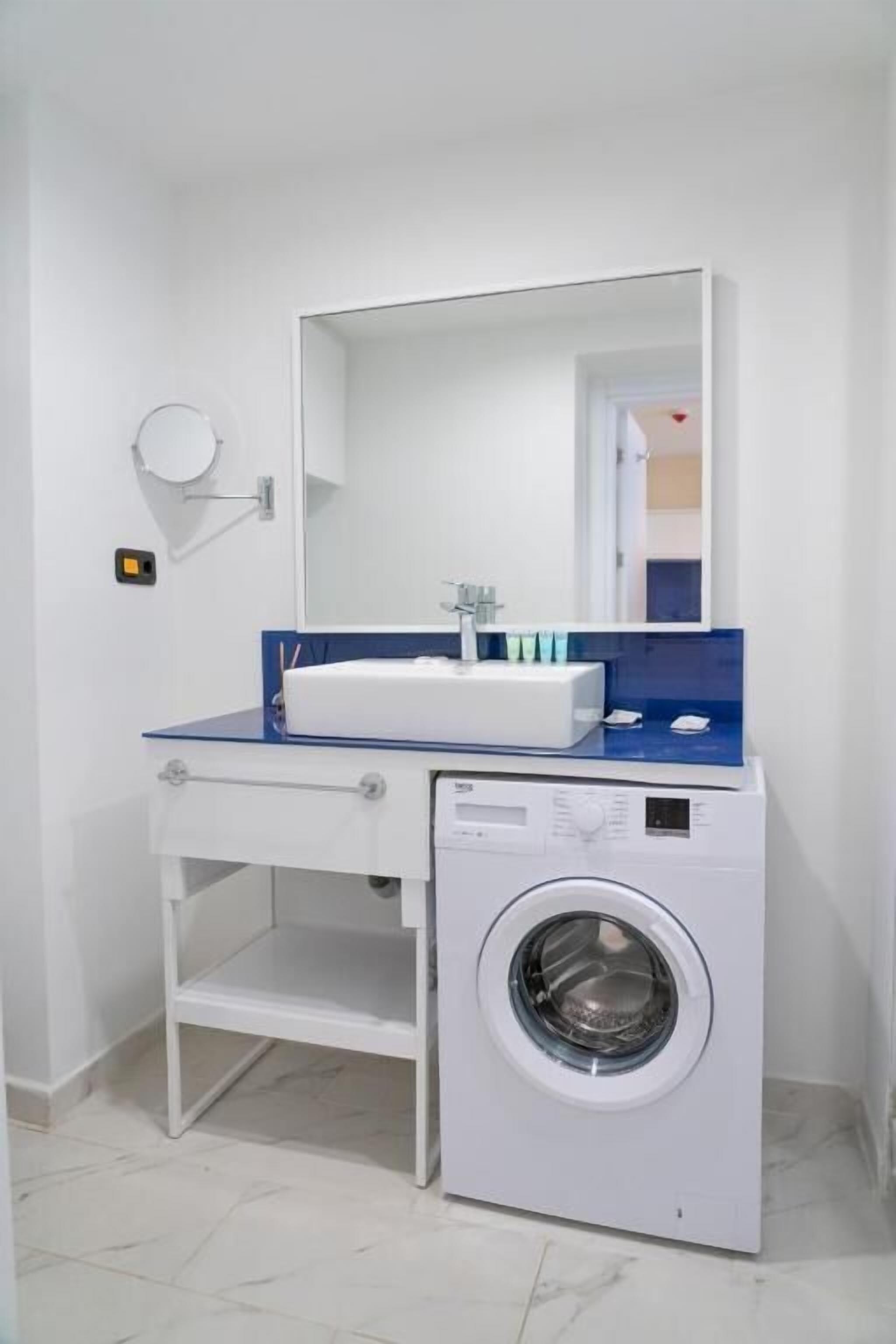 Un baño pequeño con lavamanos blanco, un espejo y una lavadora de carga frontal.