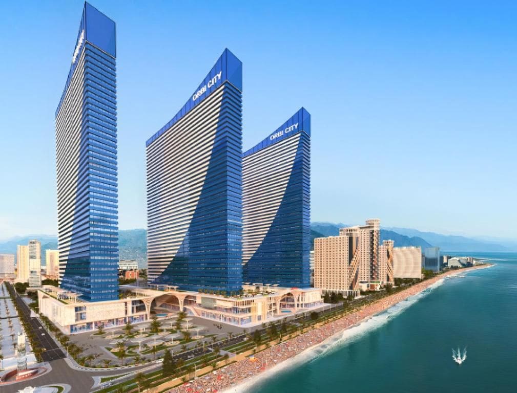 Deux gratte-ciel modernes et imposants, caractérisés par leur design ondulé distinctif, sont situés près d’une côte, à proximité d’une plage et d’un port de plaisance.