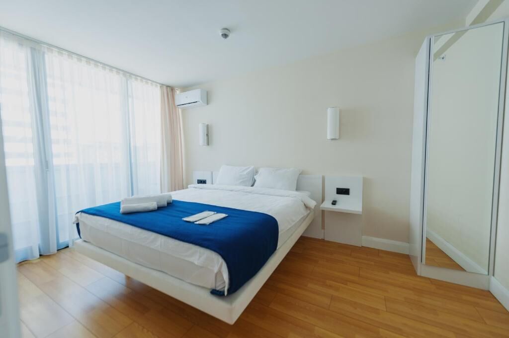 A modern hotel room with a large bed, white walls, and a wooden floor.