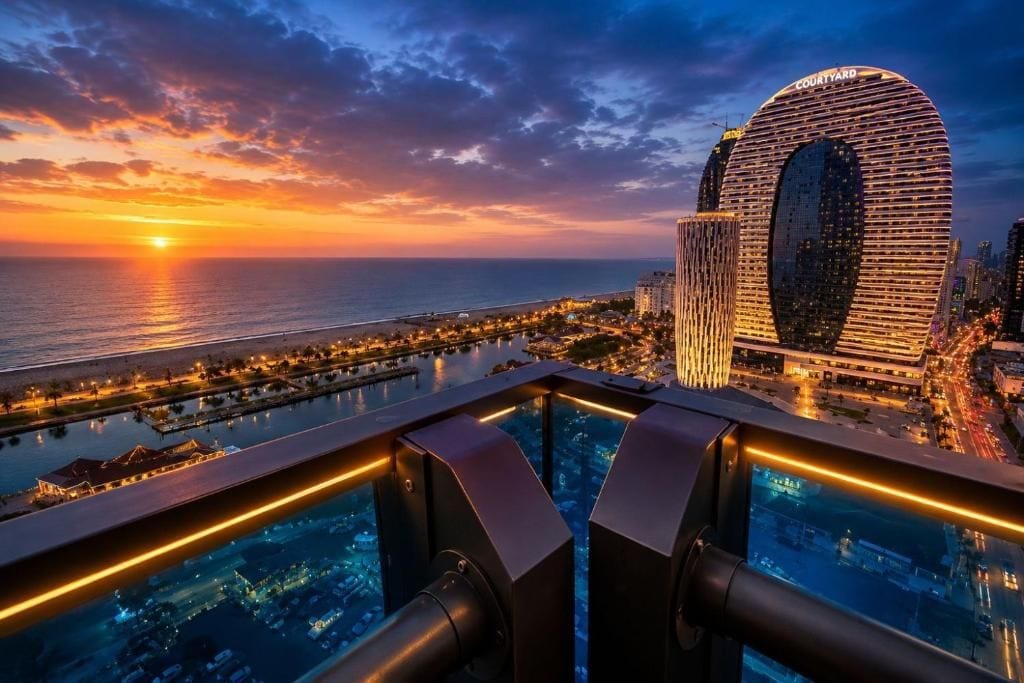 Vista panorámica de una ciudad costera al atardecer con un edificio circular destacado con el rótulo 'Courtyard' y una zona de piscina en primer plano.