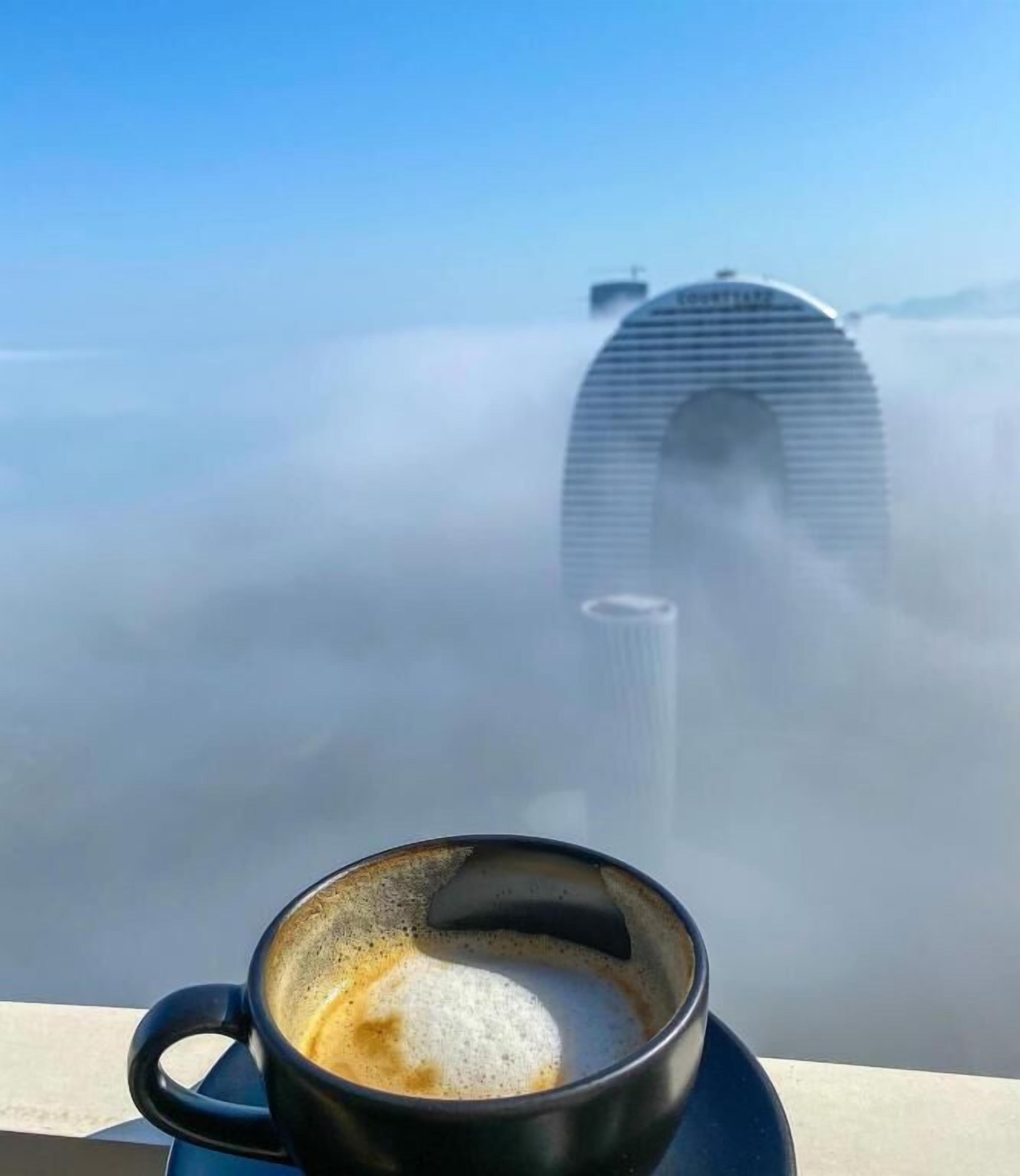A cup of coffee with a view of a building partially obscured by fog.