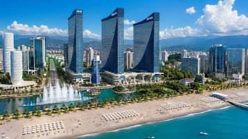 Un paysage urbain côtier avec des immeubles modernes de grande hauteur, une plage avec des transats et un ciel bleu dégagé.