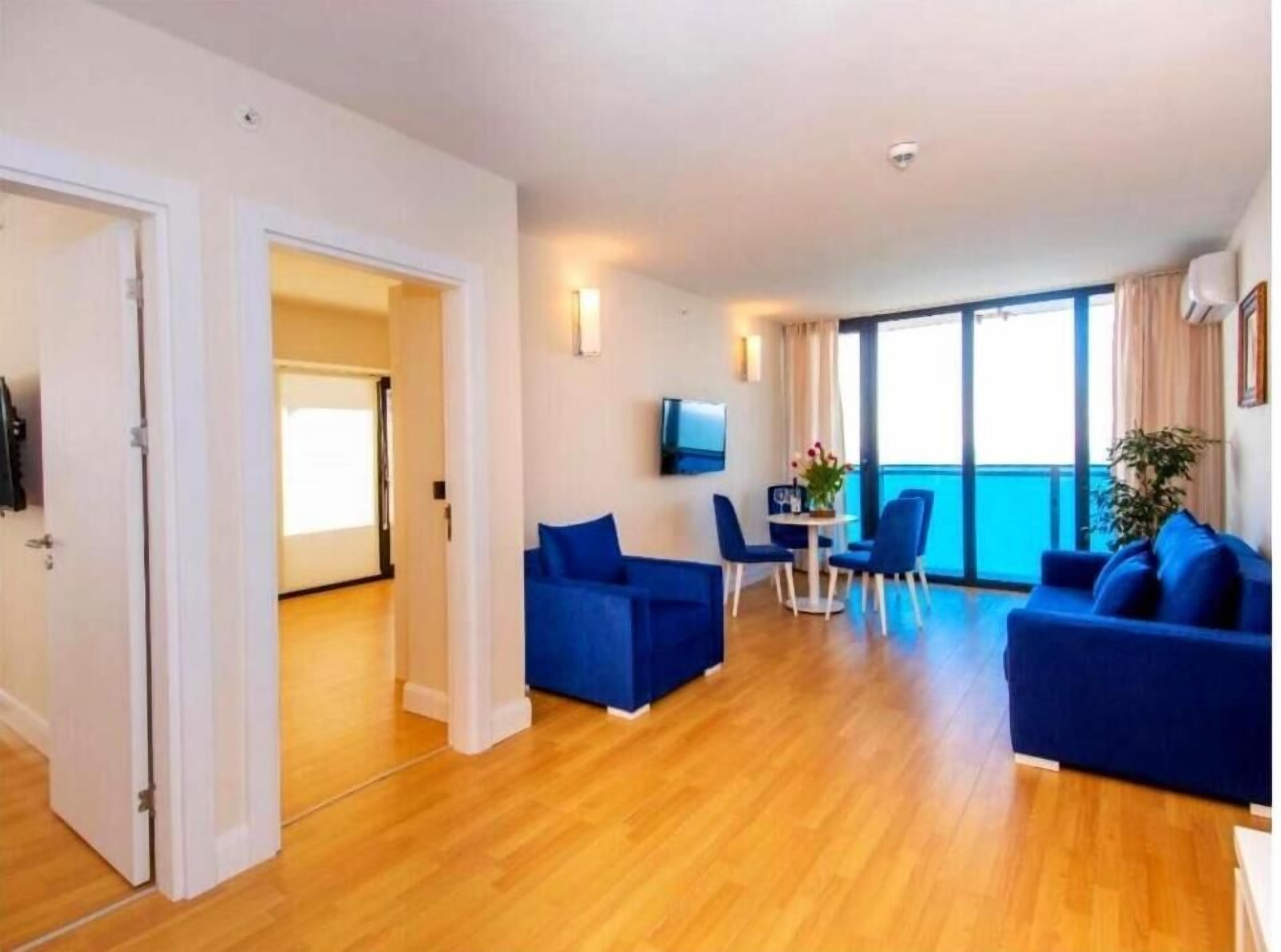 A modern living room with a sofa set, a dining area with chairs and a table, and a TV mounted on the wall.