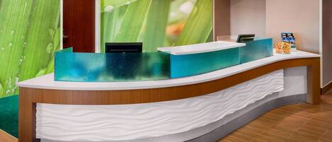 A reception desk with a green leaf wall mural, a wooden counter, and a white towel stack.