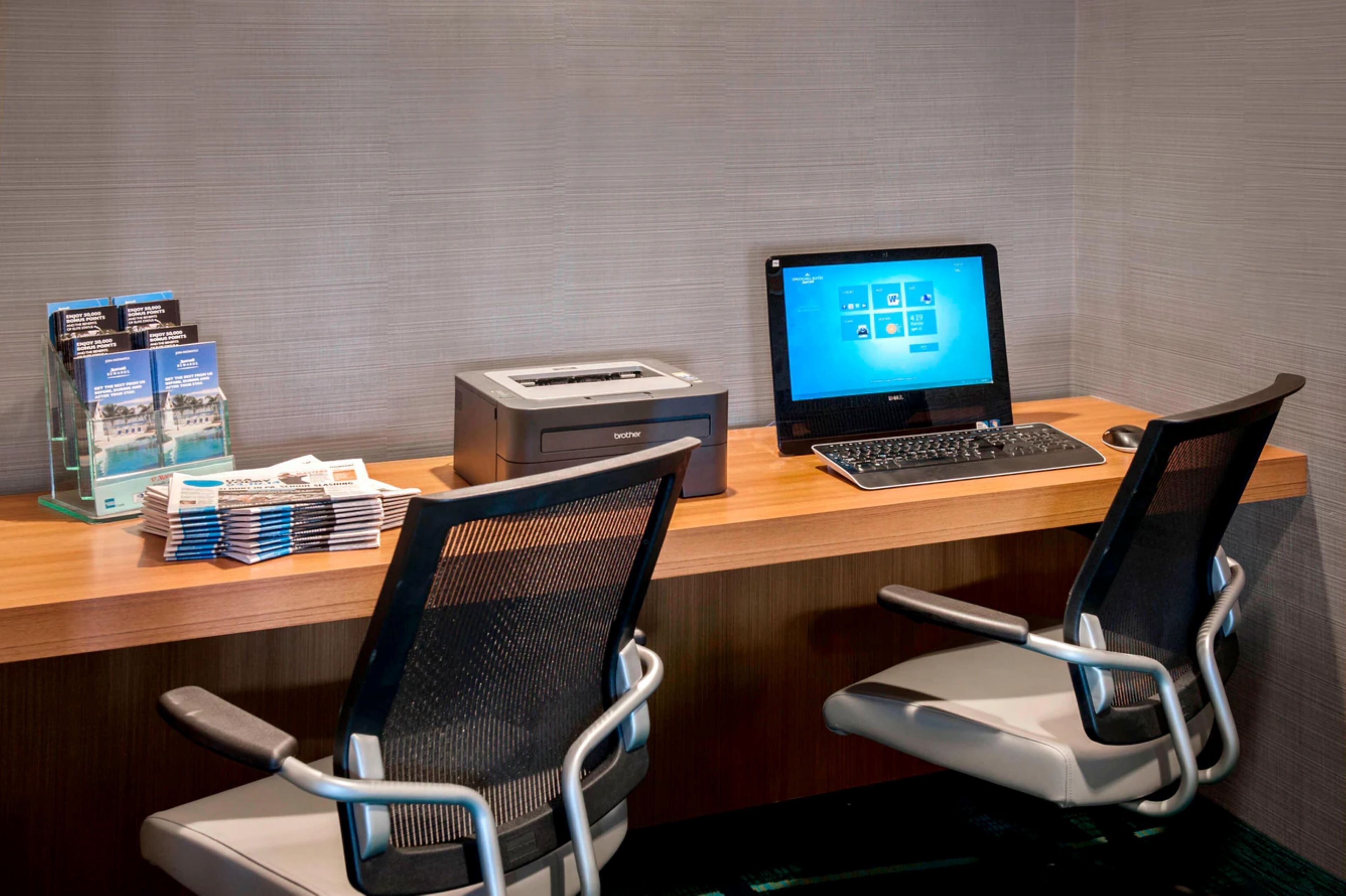 A desk with a computer, printer, and brochures. There are two office chairs.