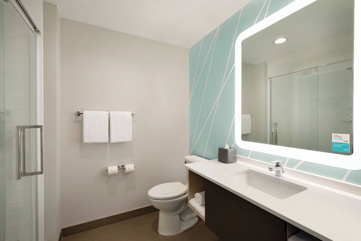 A modern bathroom with a glass shower enclosure, a white toilet, a sink with a mirror, and a towel rack.
