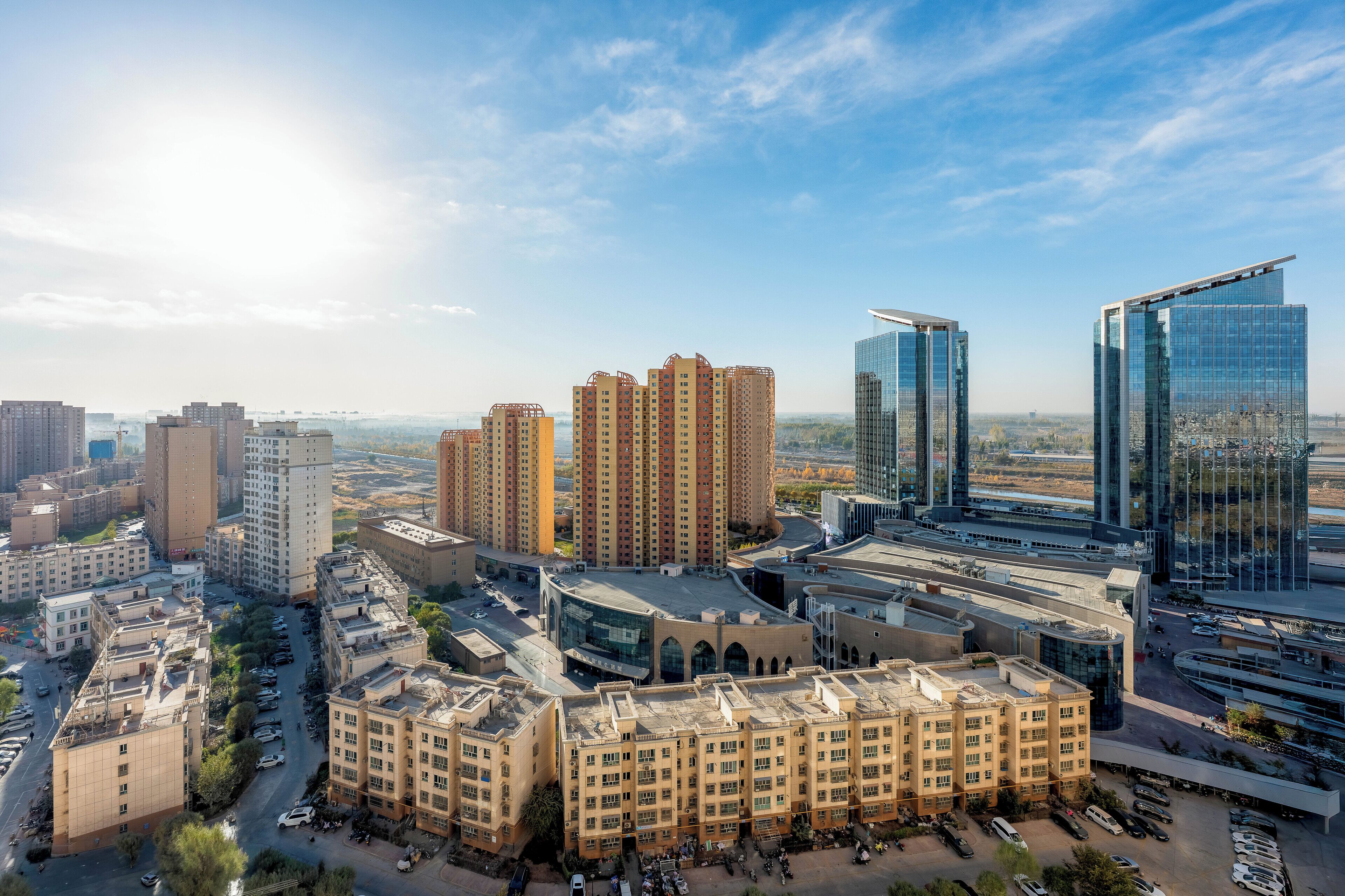 A cityscape with modern high-rise buildings, a central plaza with a large building, and a clear sky.