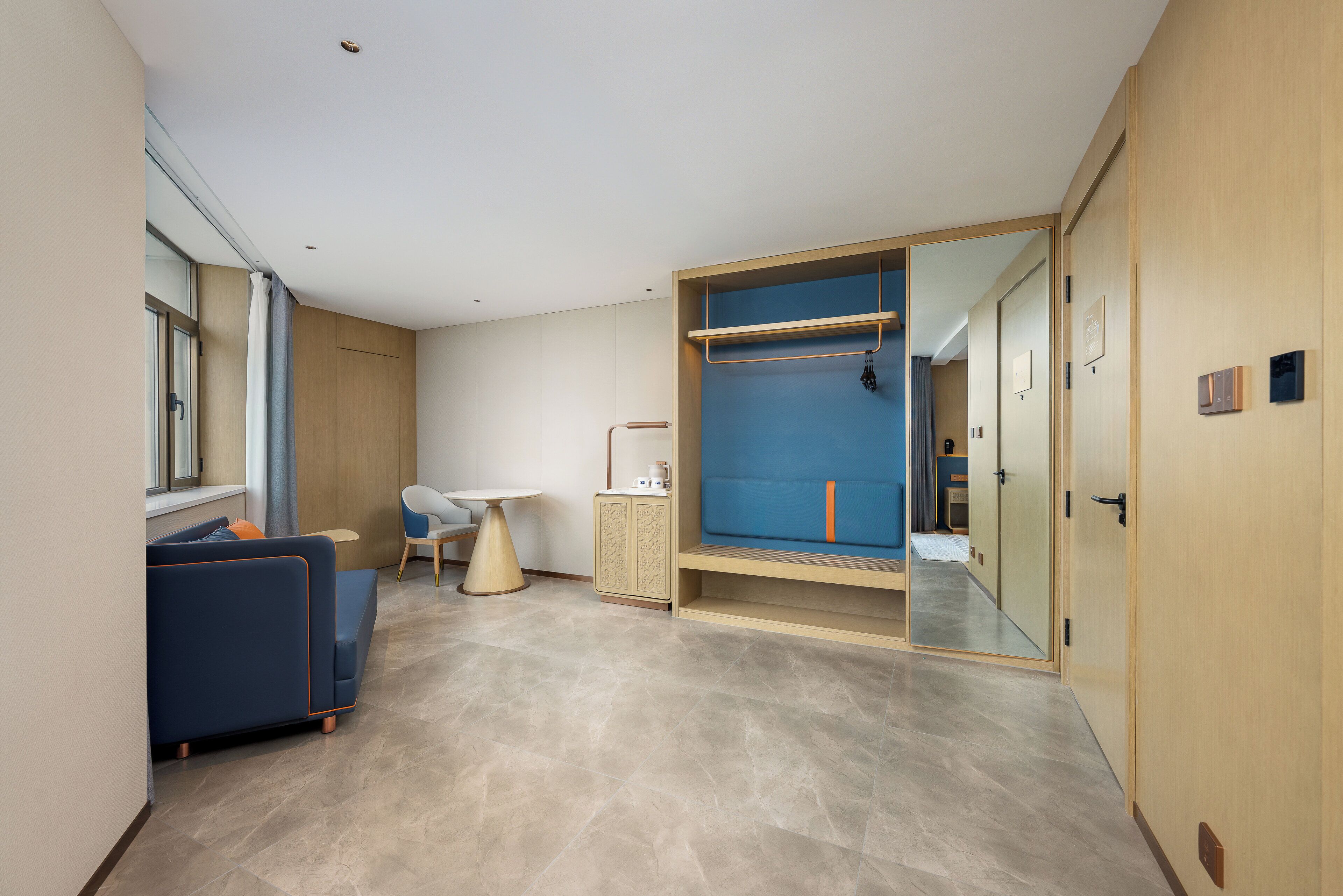 A modern hotel room with a sofa, a small table, a cabinet, and a large mirror.