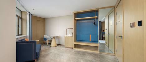 A modern hotel room with a sofa, a small table, a cabinet, and a large mirror.