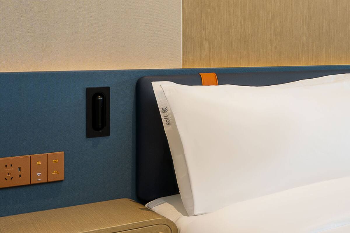 A hotel room with a bed, a power outlet, and a wall-mounted panel.