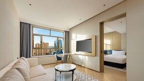 Een moderne hotelkamer met een groot raam, een bank, een ronde tafel, een bed en een televisie.
