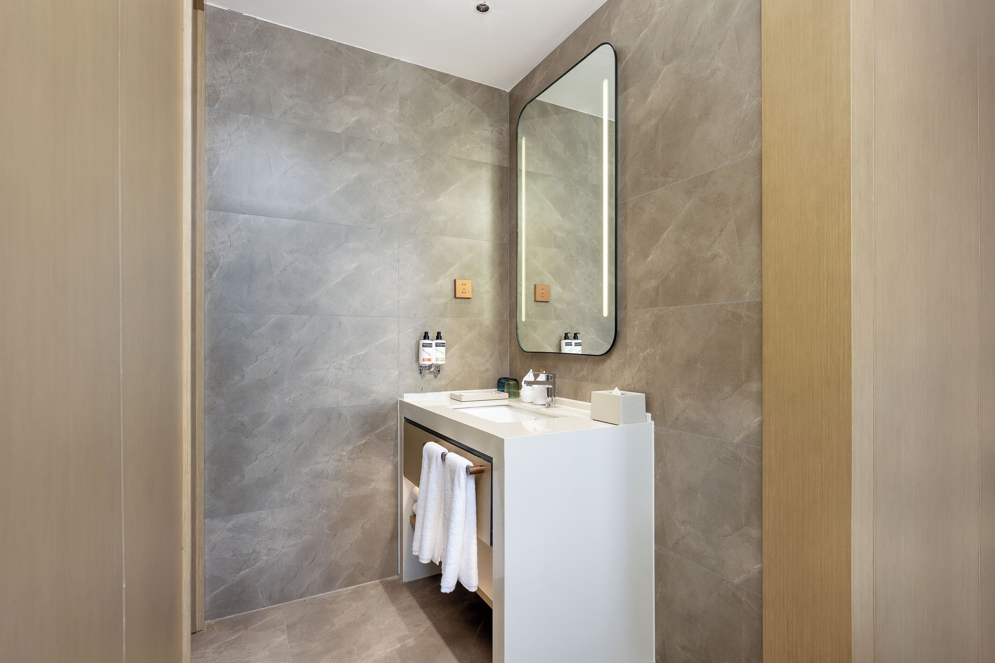 A modern bathroom with a large mirror, a white sink, and a towel rack.