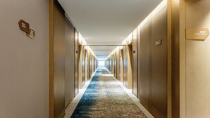Een hotelgang met een kamerbreed tapijt, houten wanden en een bordje met daarop de liftlobby.
