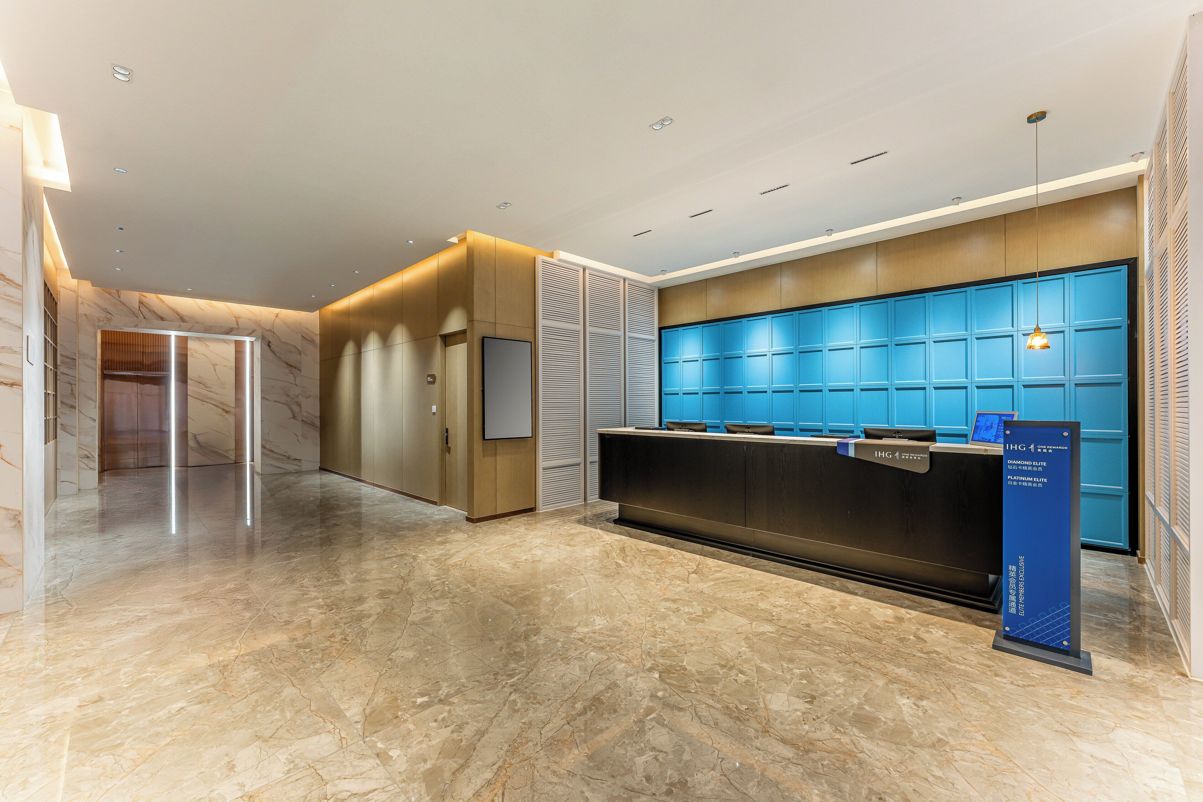 Un área de recepción moderna con suelo de mármol, una mesa de recepción y una pared azul con pantalla digital.