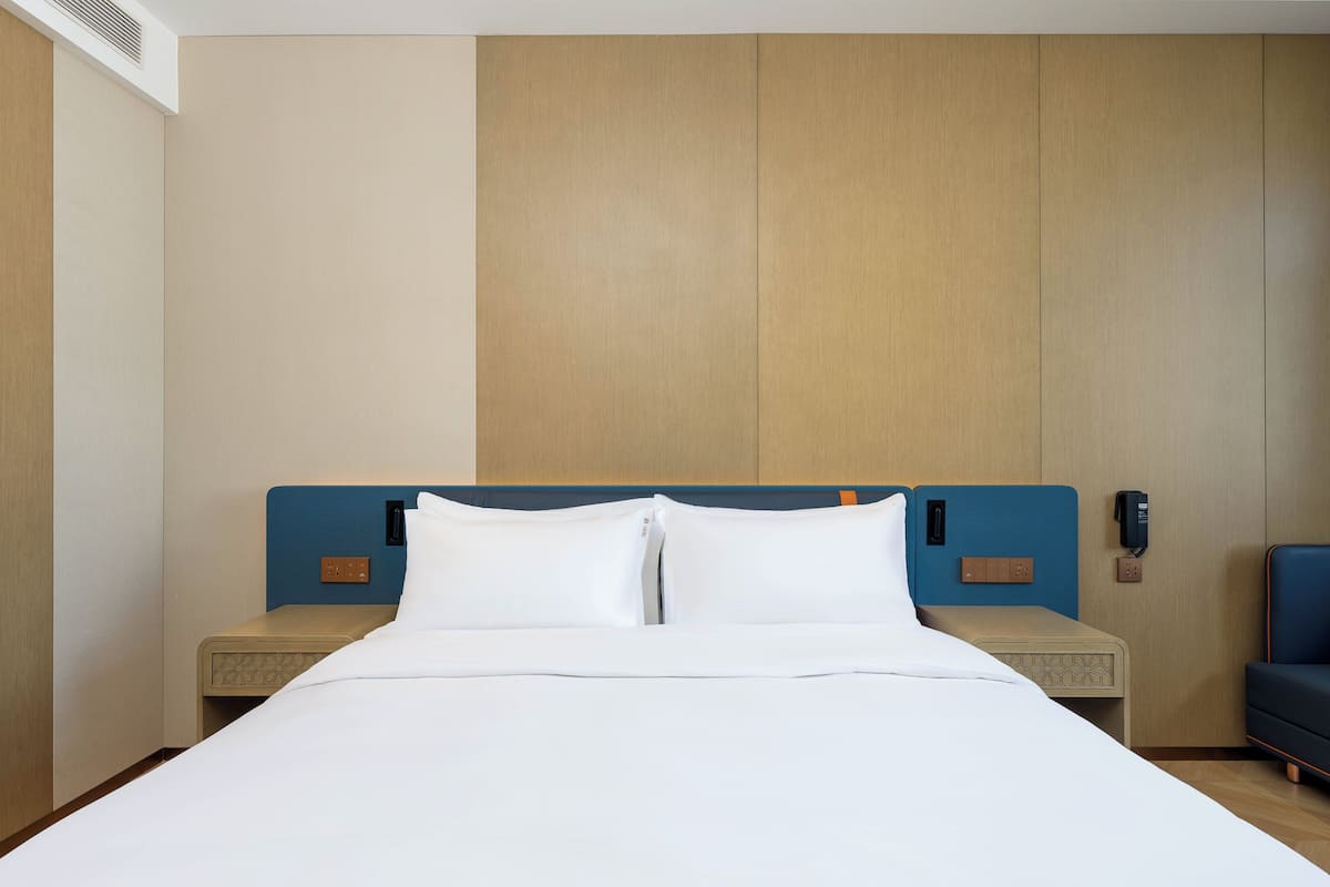 A hotel room with a large bed, a blue headboard, bedside tables, a phone, and a small seating area.