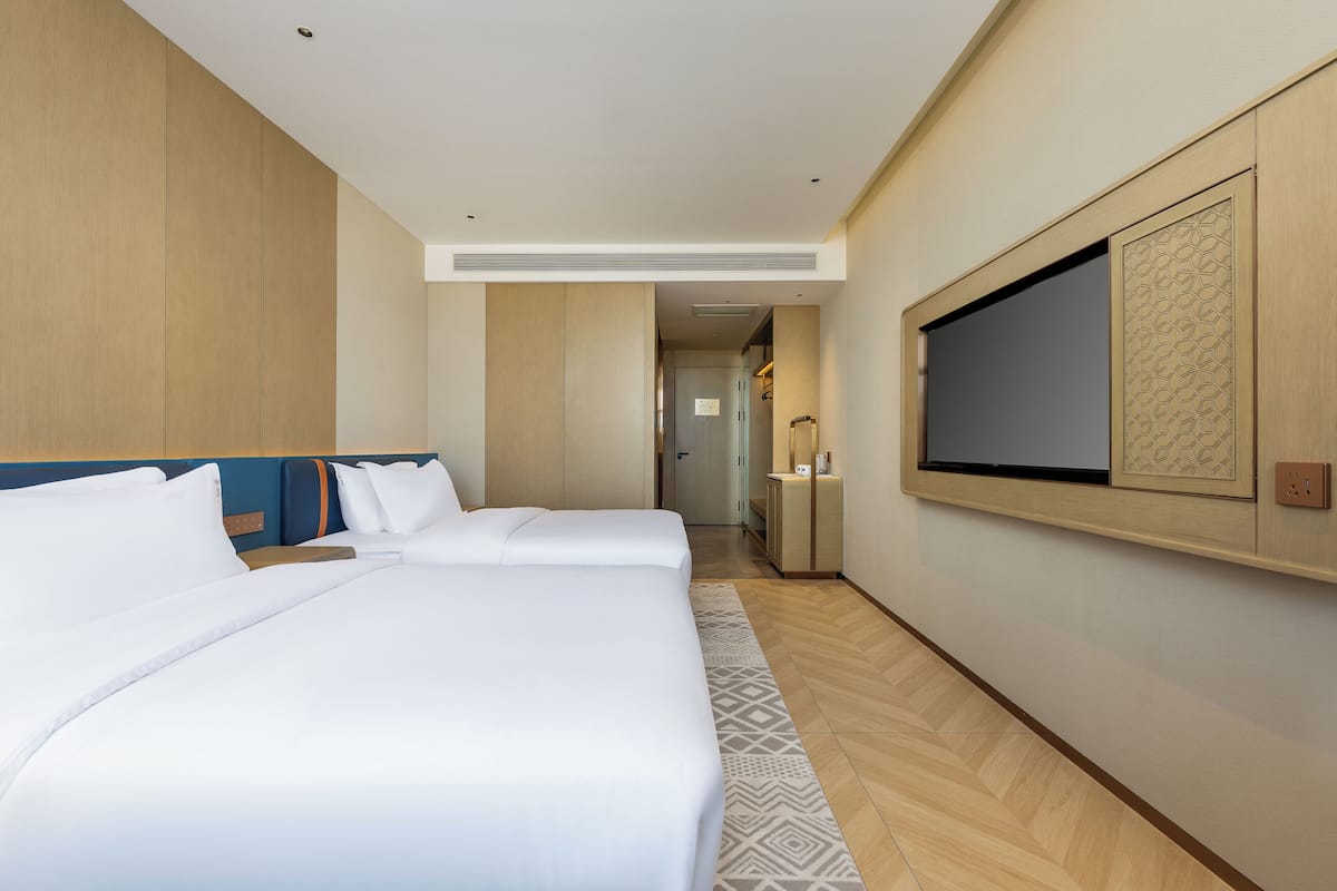 A hotel room with two beds, a TV, and a hallway leading to a bathroom.