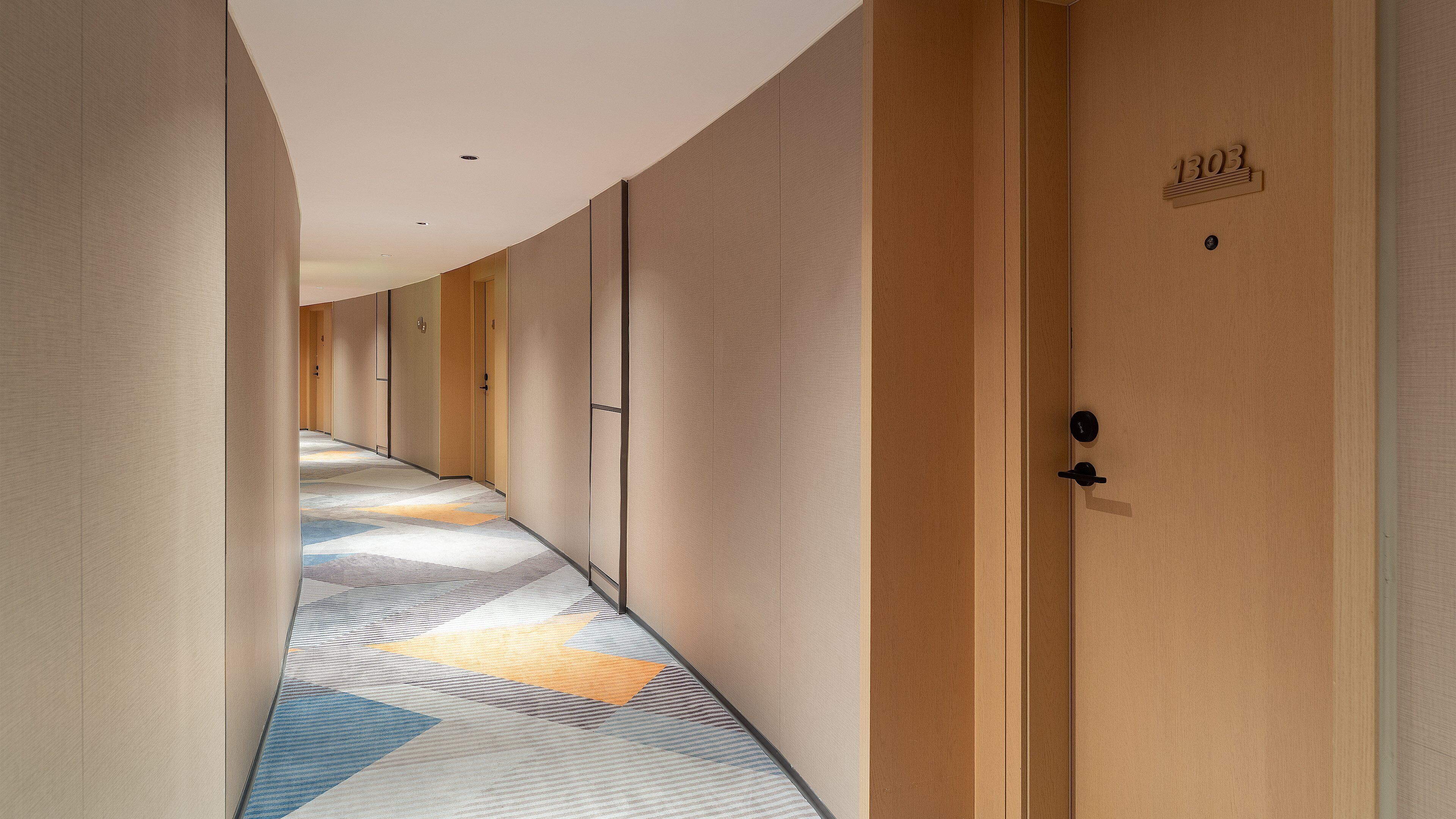 A hotel corridor with wooden doors, numbered 1303, and a patterned carpet.