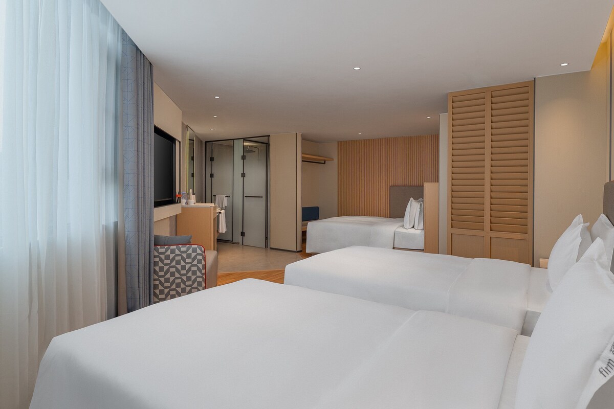 A hotel room with two beds, a desk, a chair, and a wardrobe.