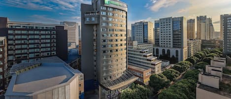 A modern hotel with a prominent sign, surrounded by high-rise buildings and greenery.