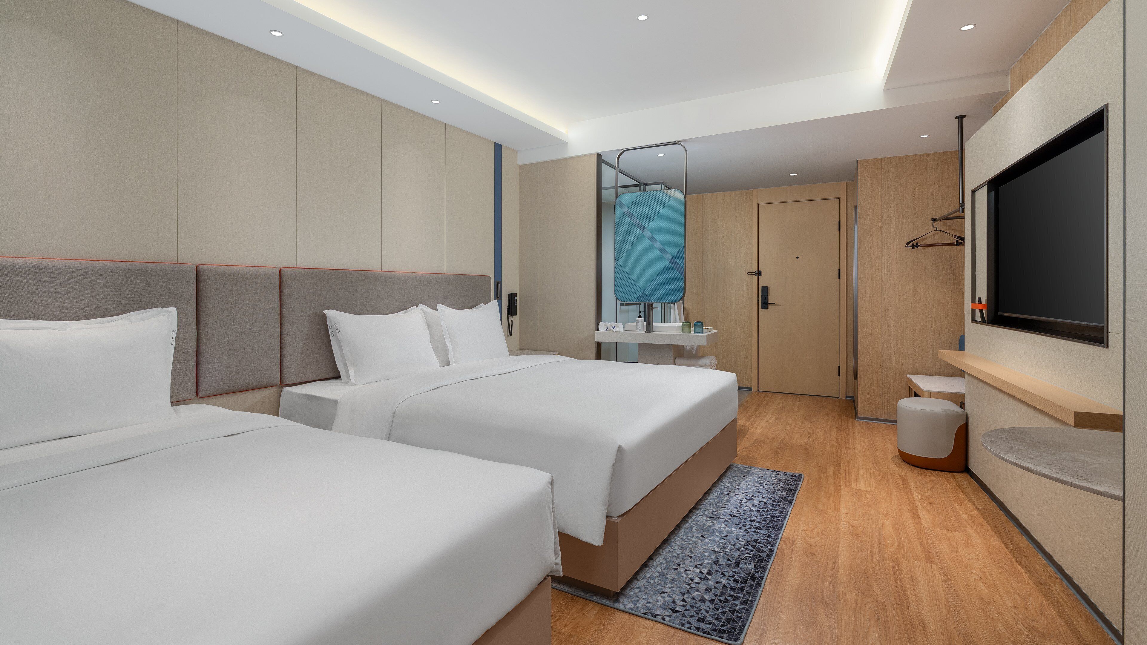 A modern hotel room with two beds, a TV, a mirror, and a bathroom.