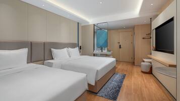 A modern hotel room with two beds, a TV, a mirror, and a bathroom.