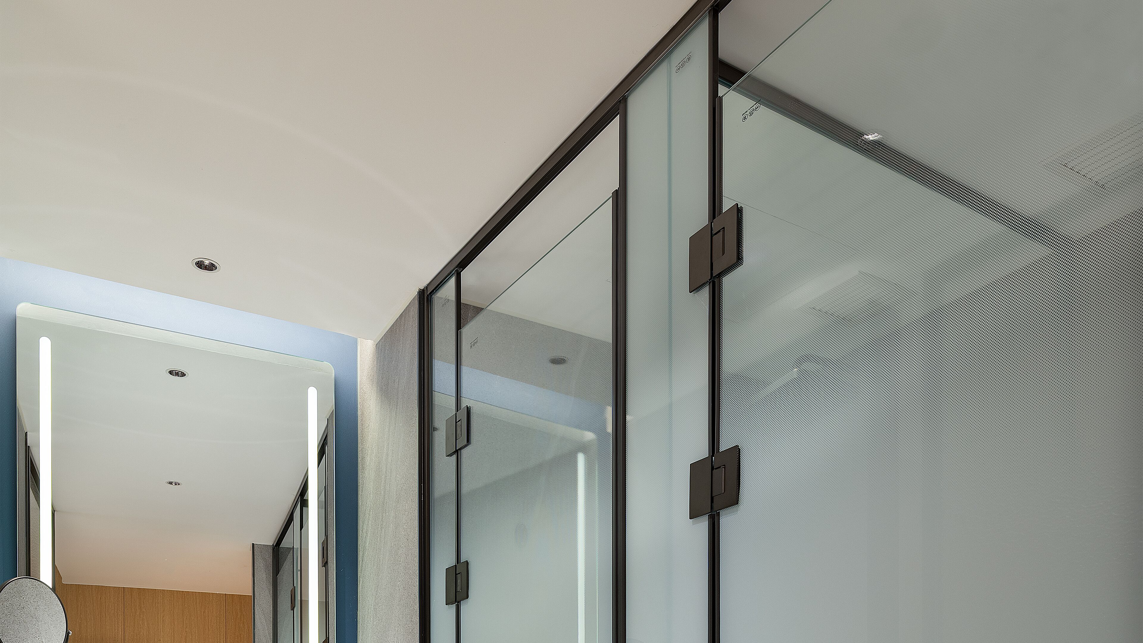 A modern interior with a glass partition, a visible door, and a ceiling with recessed lighting.