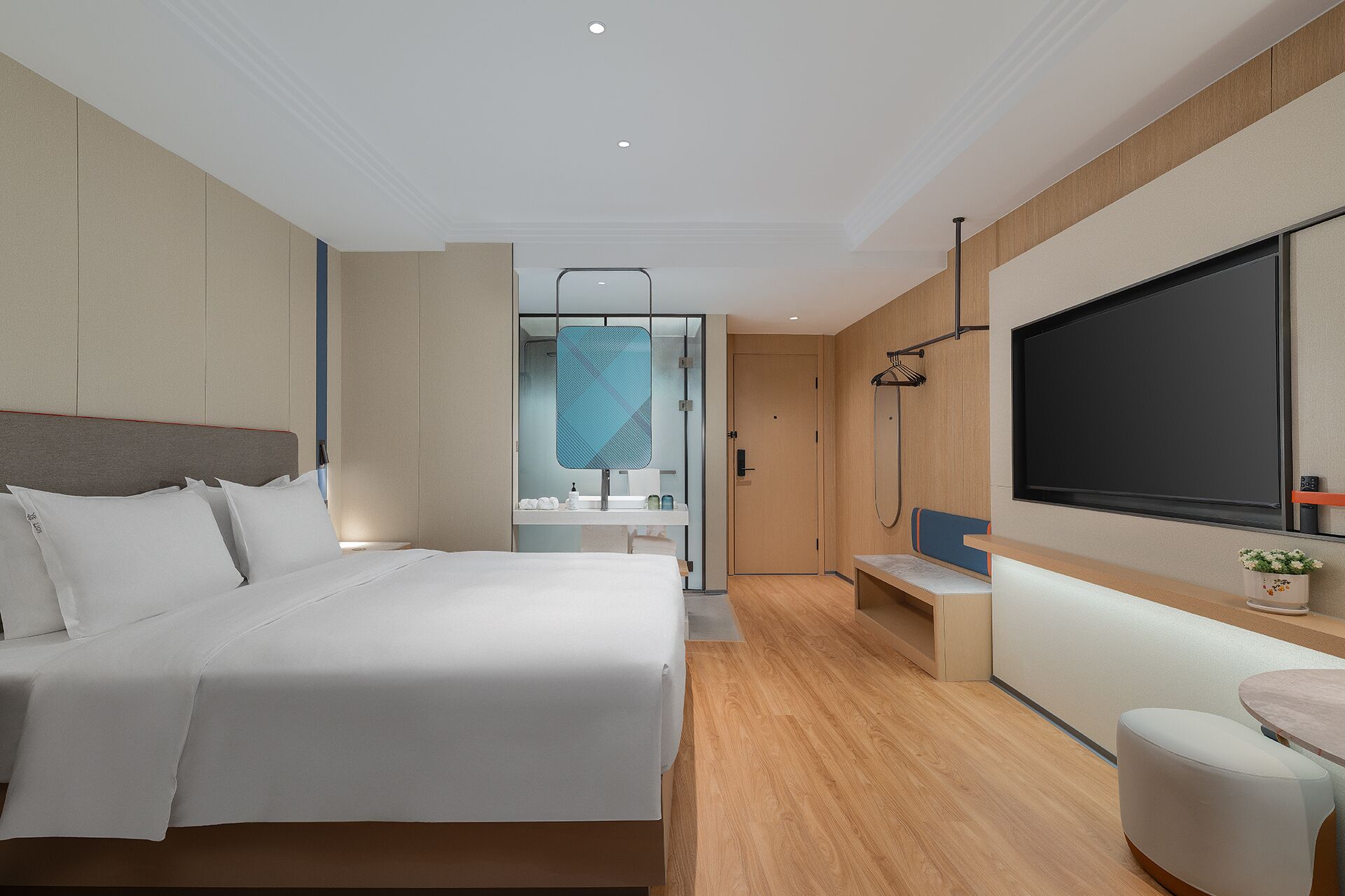 Habitación de hotel moderna con una cama grande, un escritorio, un televisor y un baño visible a través de una pared de vidrio.