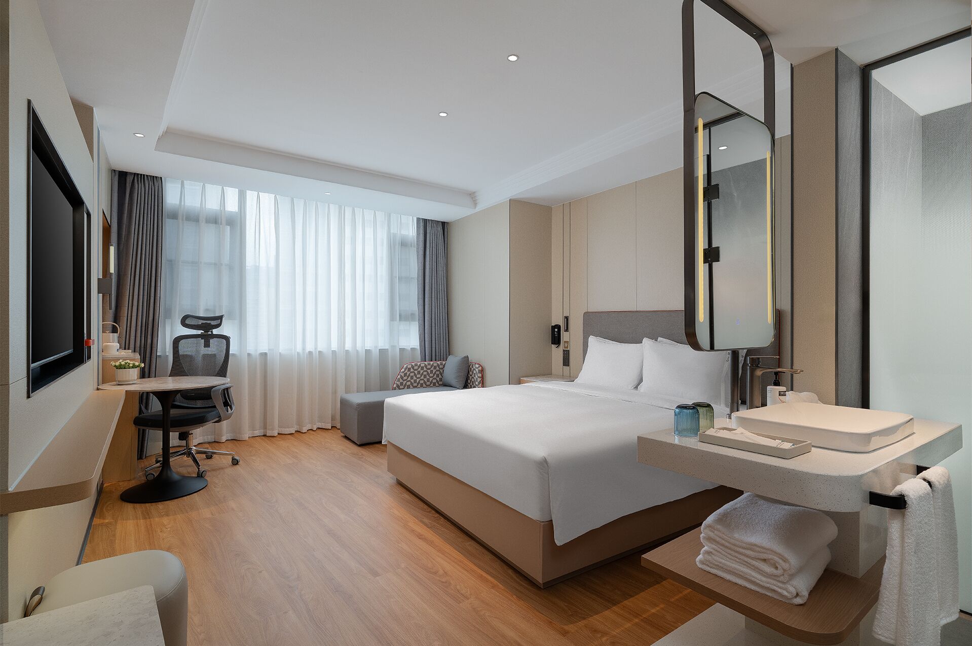 A modern hotel room with a large bed, a desk with a chair, a bathroom with a sink and mirror, and a large window with curtains.