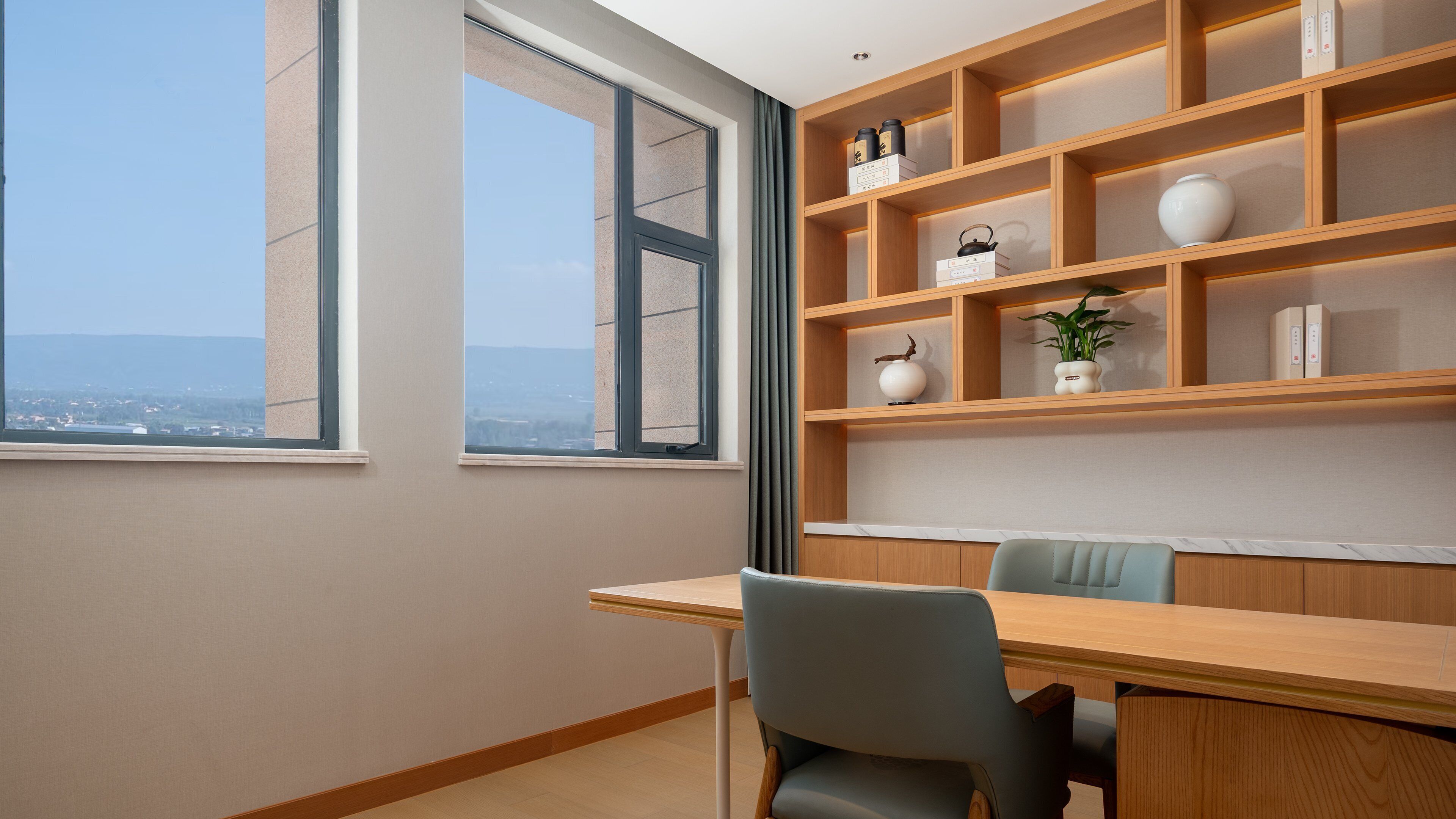 A room with a large window, a wooden desk, a chair, and a built-in shelving unit with decorative items.