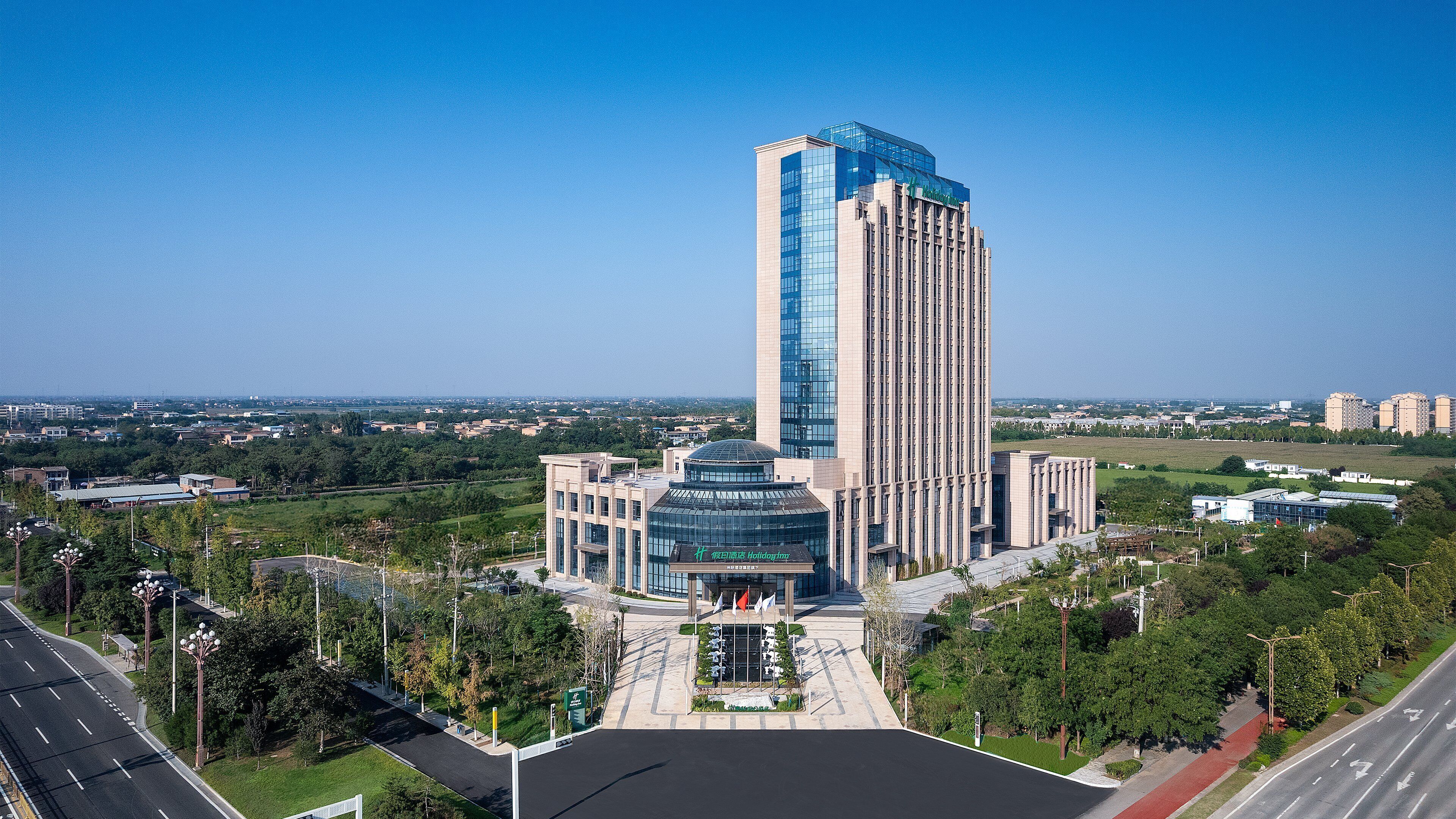 A high-rise hotel with a modern glass facade, surrounded by greenery and a clear sky.