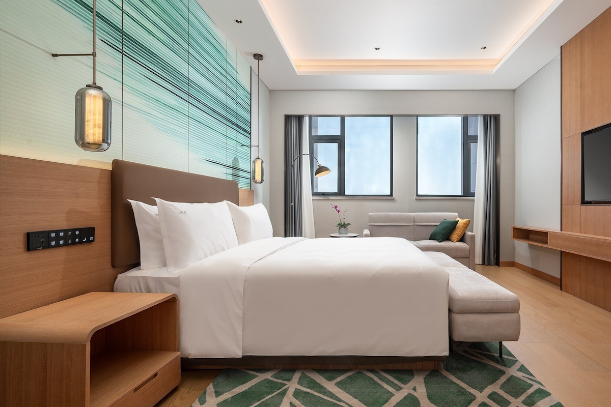 Una habitación de hotel moderna con una cama grande, un sofá, un televisor y un escritorio.