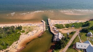 Vista aérea de una playa con un muelle, zonas arenosas y un pequeño edificio.