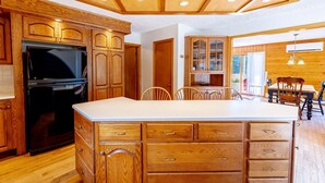 Una cocina con armarios de madera, un refrigerador negro, un comedor con sillas de madera y una isla grande con cajones.